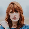 A red-haired woman with tattoos standing in a field.